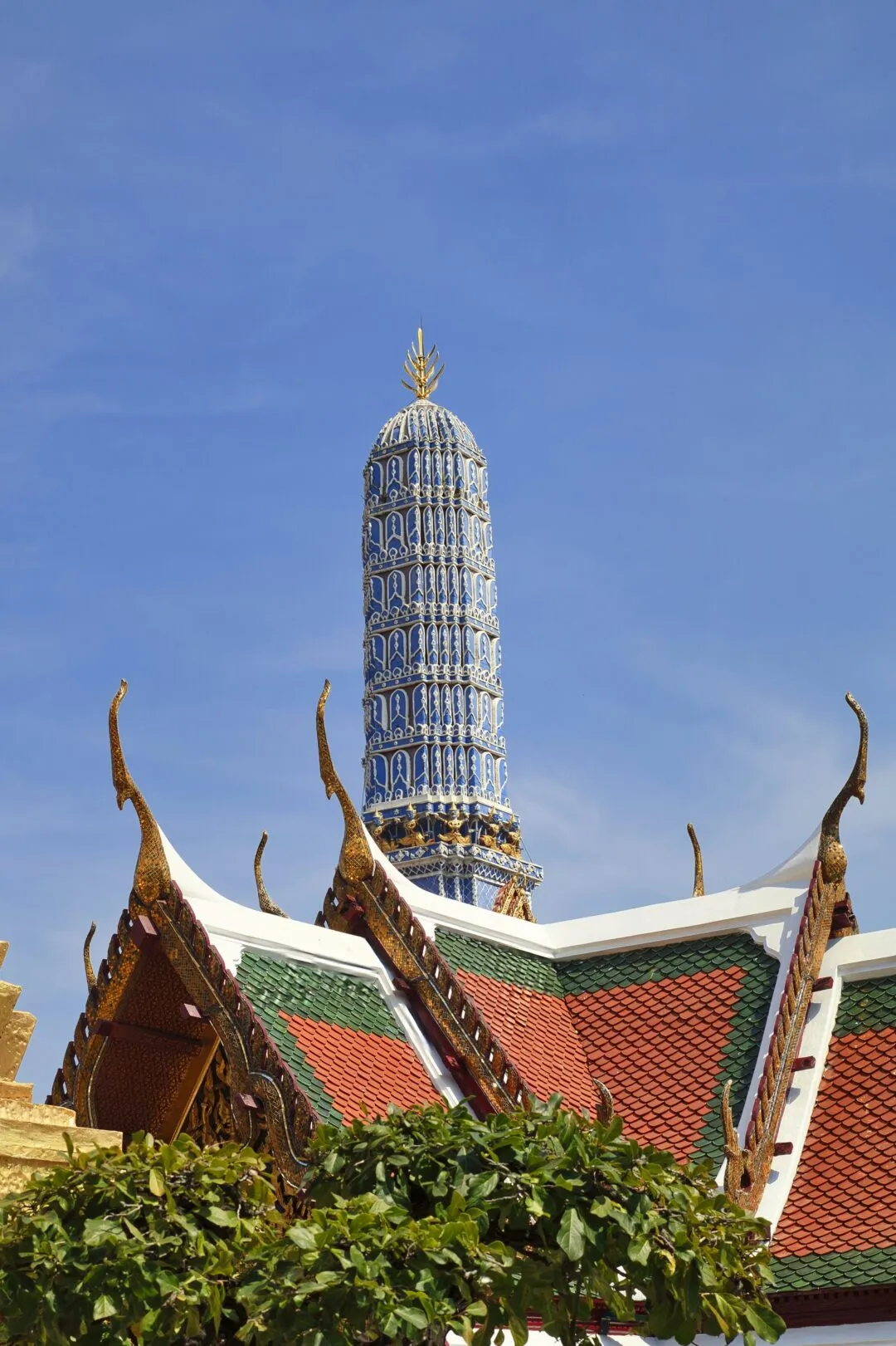 A porcelain-tiled temple spire rising over a green-tiled naga roofline in Bangkok.