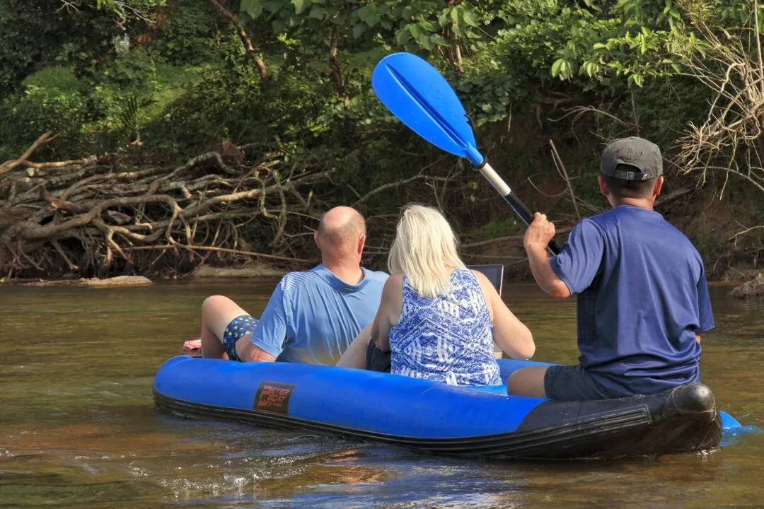 A rafter paddling down a jungle river in Thailand, paddle raised mid-stroke.