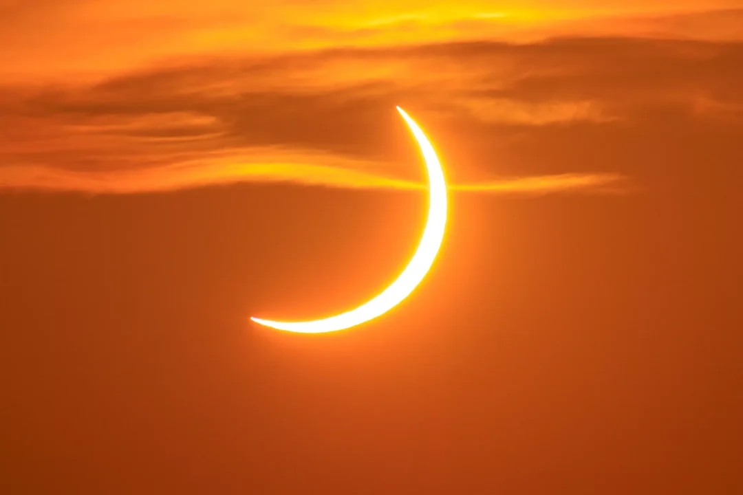 A sharp, thin crescent of the eclipsed sun in a clear orange evening sky over Ibiza