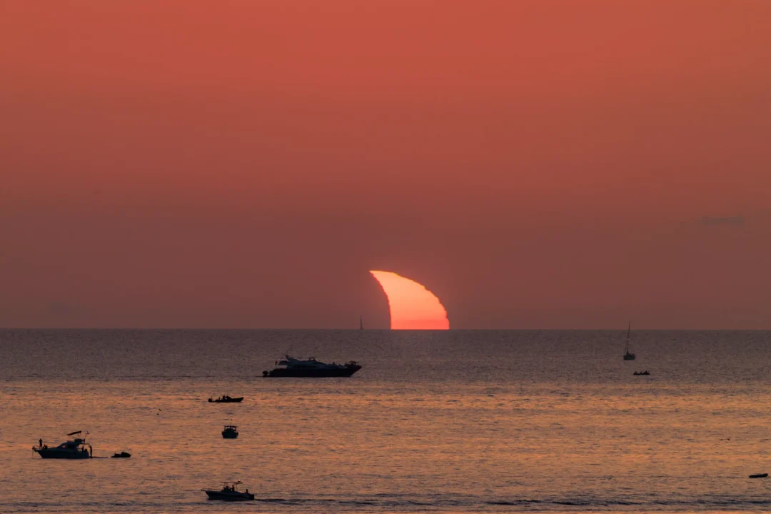 The last thin sliver of the eclipsed sun glowing just above the horizon over a scattering of small boats off Ibiza