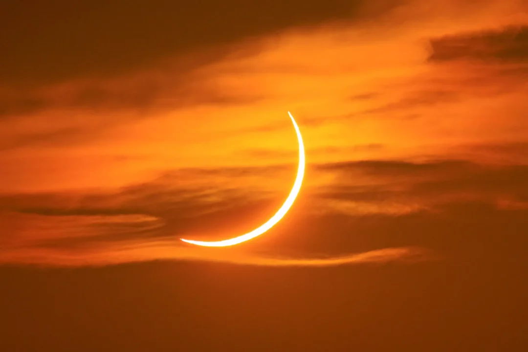 A bright white crescent sun set against a vivid orange sunset sky streaked with clouds over Ibiza