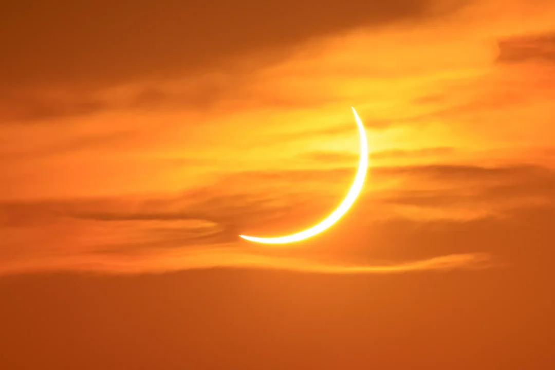 The eclipsed crescent sun glowing through wispy orange clouds low over Ibiza at sunset