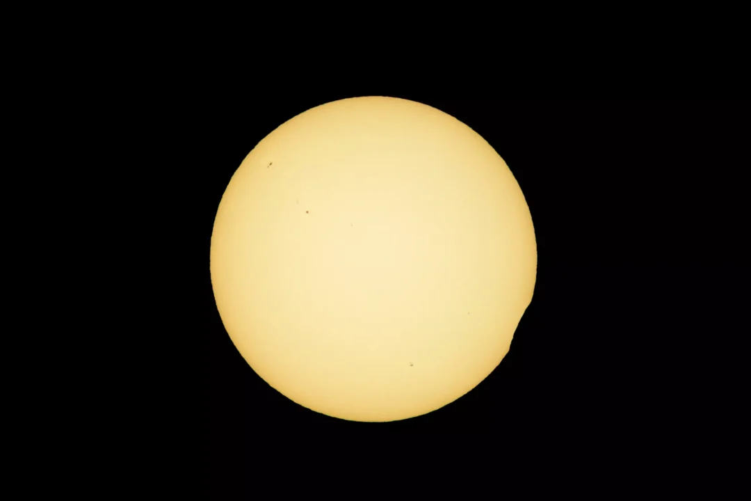 The Moon beginning to cross the Sun's disc, a small dark bite visible at the edge, marking the start of the partial solar eclipse over Ibiza