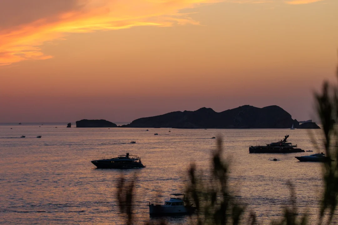 The eclipsed sun's glow fading below the horizon at sunset, silhouetted boats on the calm sea off Ibiza