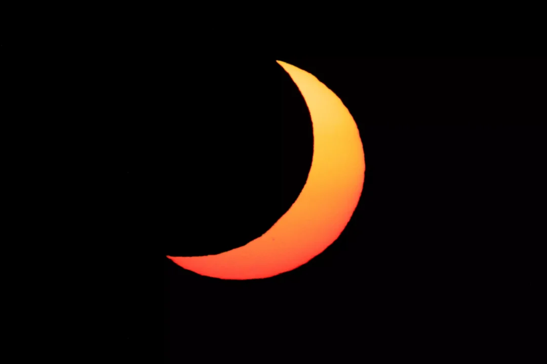 A deep orange crescent sun low in the sky as it descends towards the horizon during the Ibiza eclipse