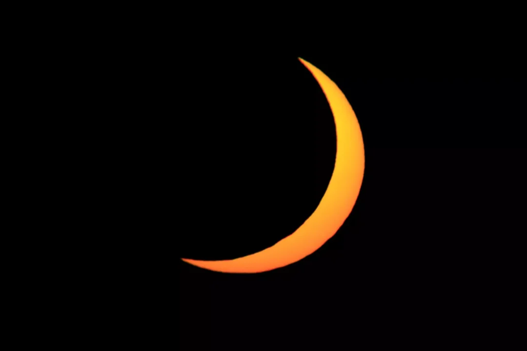 A high-contrast sliver of the eclipsed sun against a near-black dusk sky above Ibiza