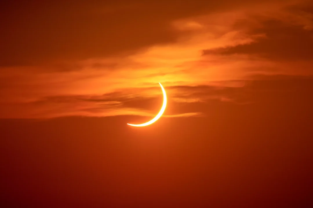 A slender crescent of the eclipsed sun glowing through streaks of cloud low in the sky over Ibiza