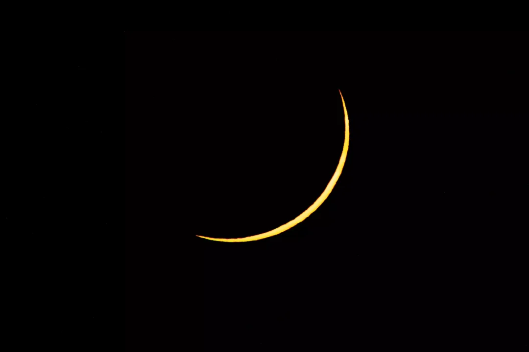 A thin, sharply defined crescent of sunlight against a black sky, captured through a solar filter during the Ibiza eclipse