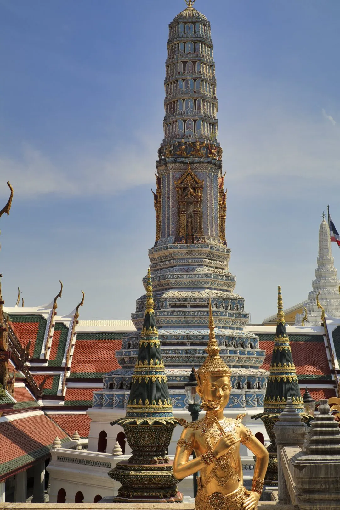 A tall tiered prang tower framed by a golden mythological kinnari figure in Bangkok.