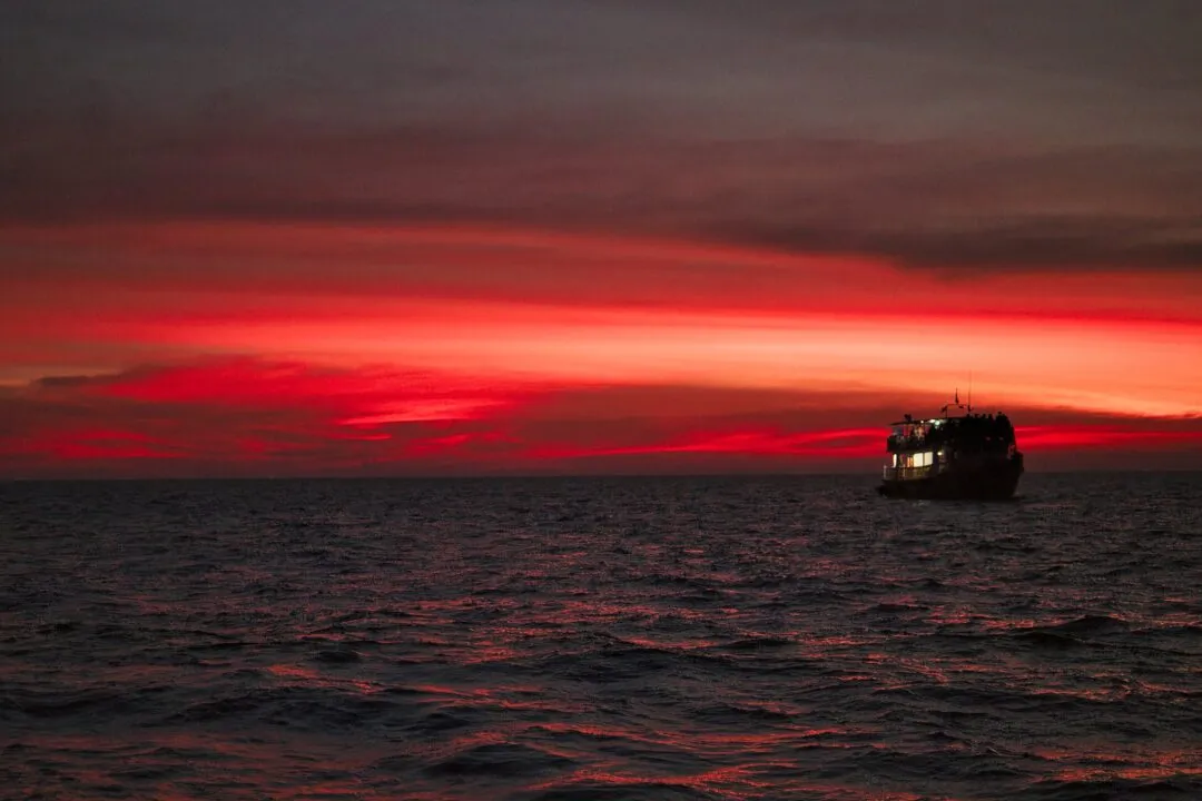A tour boat silhouetted against a deep red sunset sky on the Thai coast.
