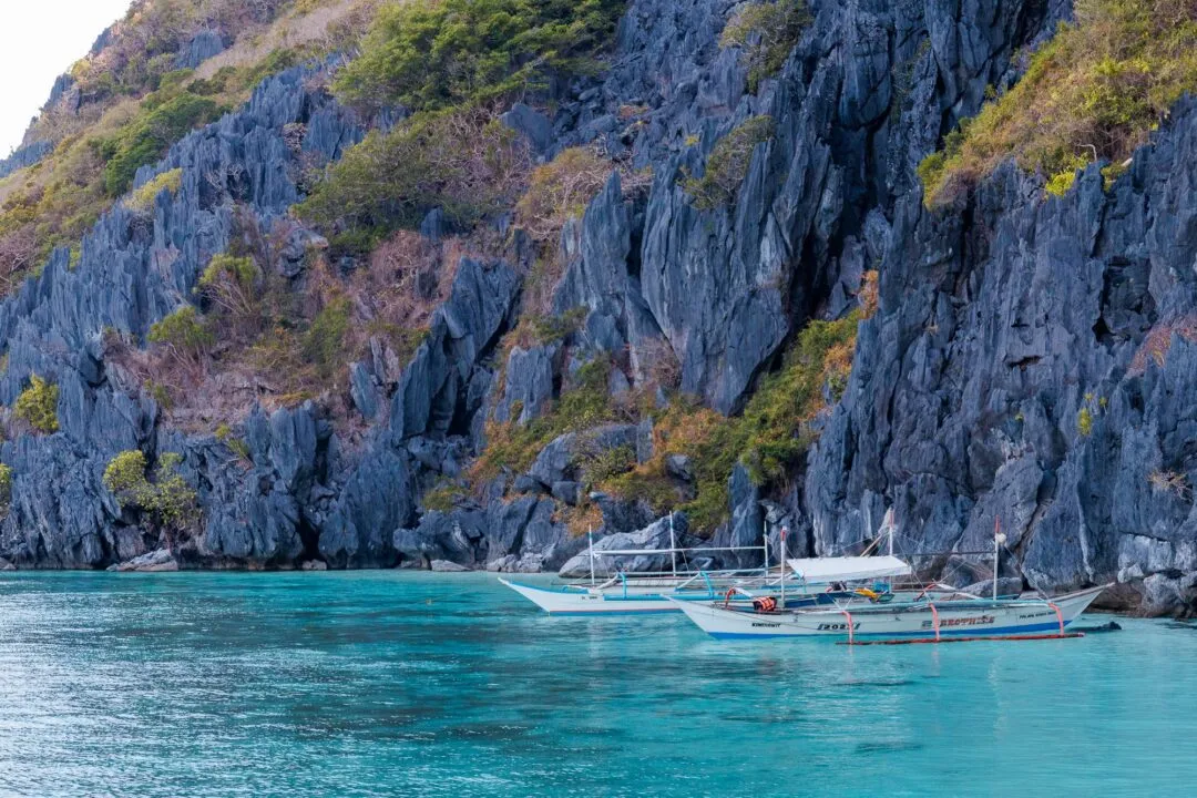 Turquoise lagoon two banca boats towering cliff El Nido